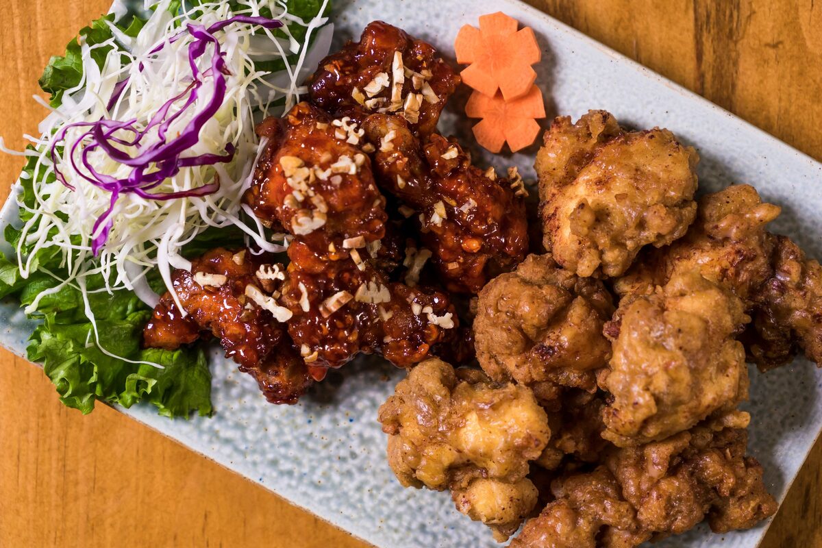 A platter of Korean fried chicken, half glazed in sweet-spicy sauce with sesame and half plain crisp, beside shredded cabbage