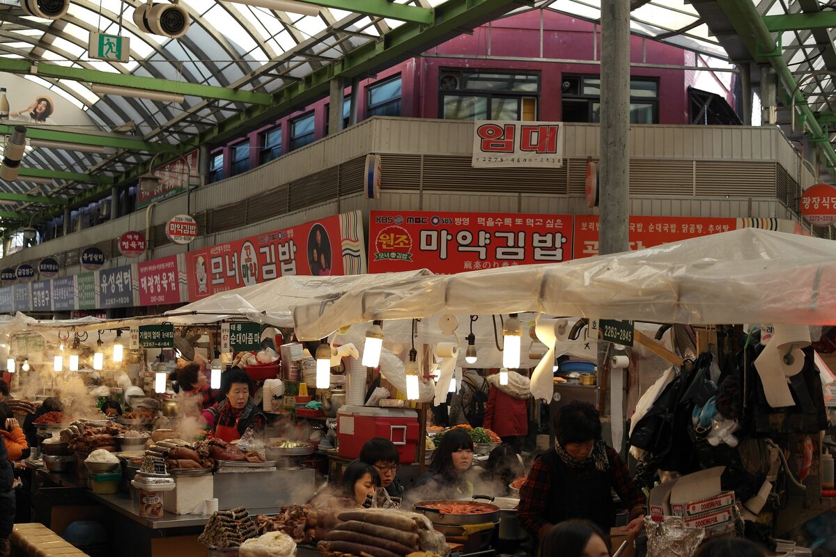 Food stalls under the roof of Gwangjang Market, with vendors and shoppers packed along the aisles