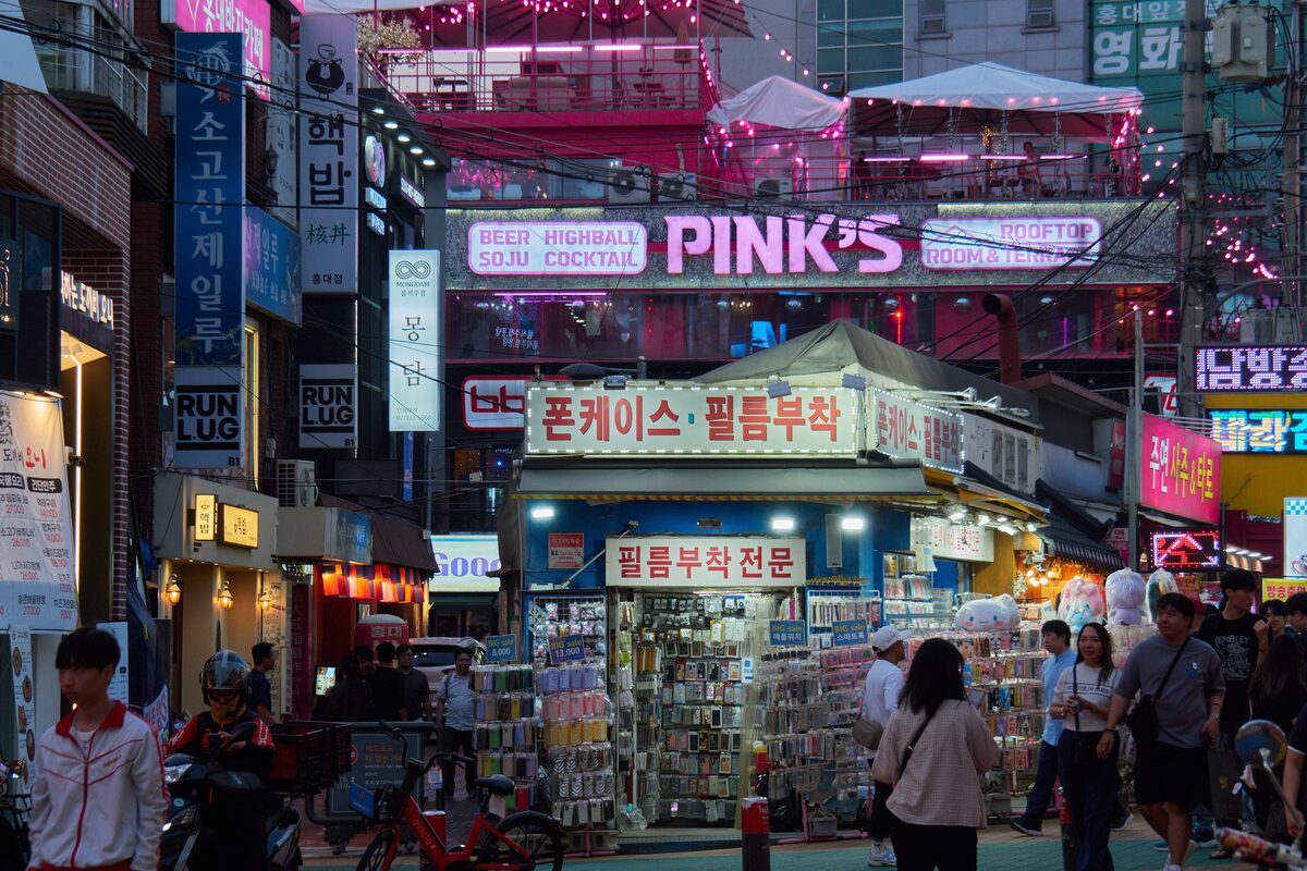 A busy Hongdae street with bright neon signs, a phone accessory shop and crowds of people