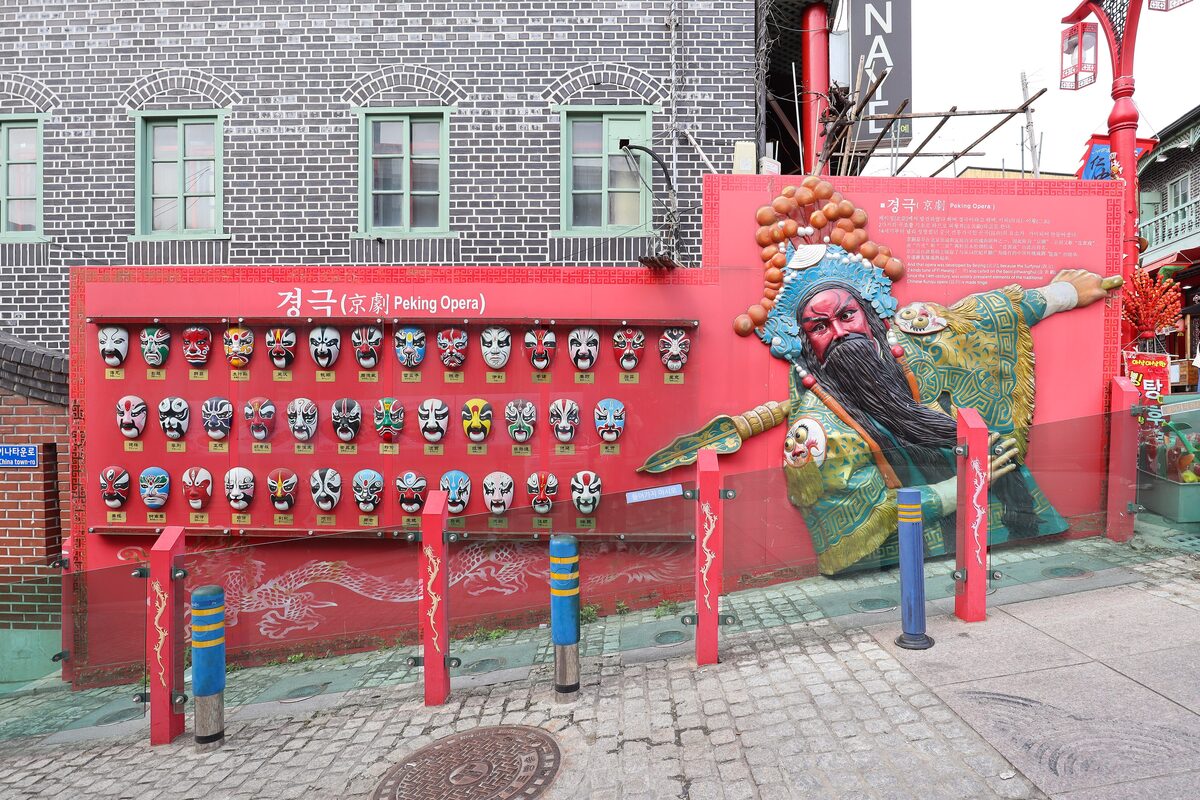 A red wall with rows of Chinese opera masks and a painted opera figure in Incheon's Chinatown