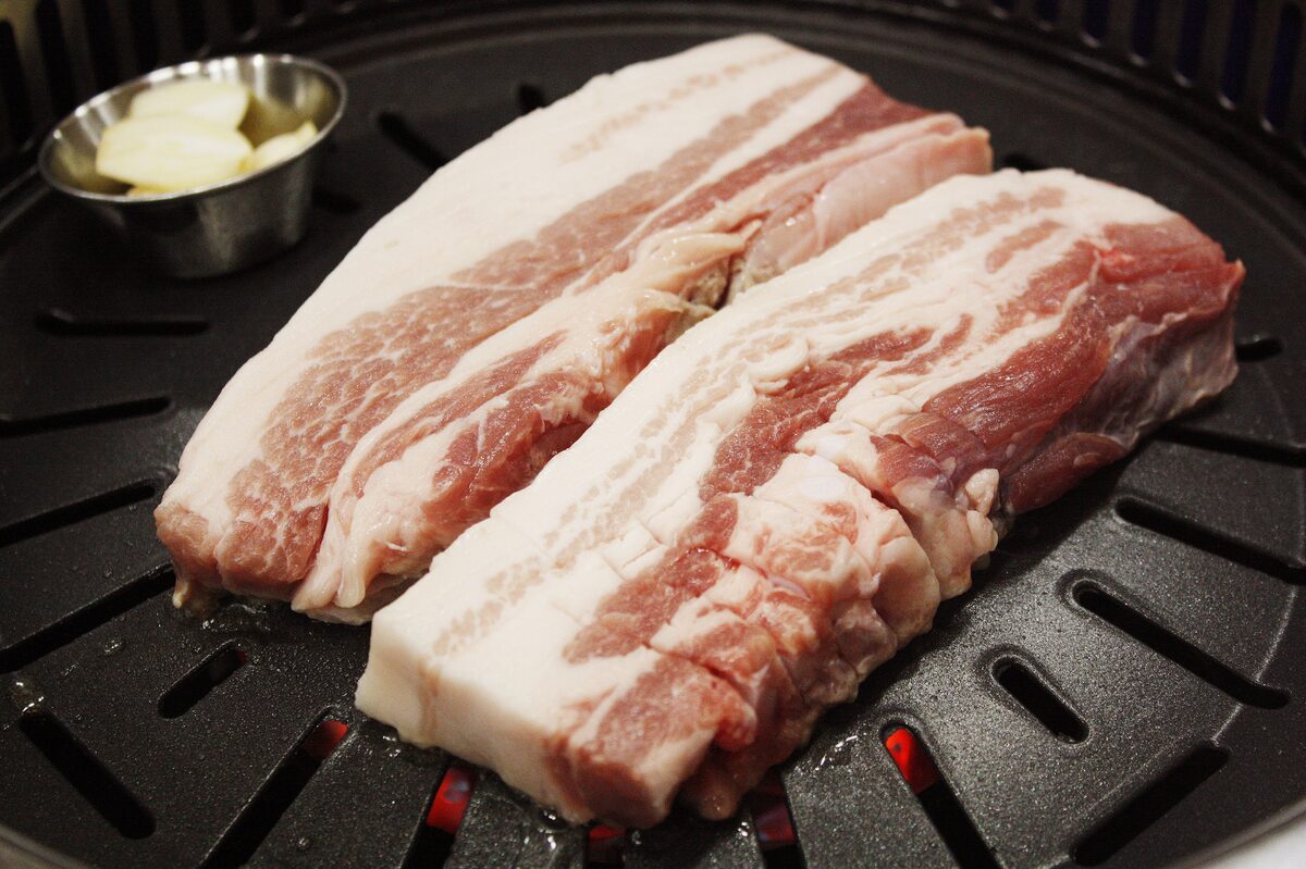Two thick slices of raw pork belly laid on a Korean table grill