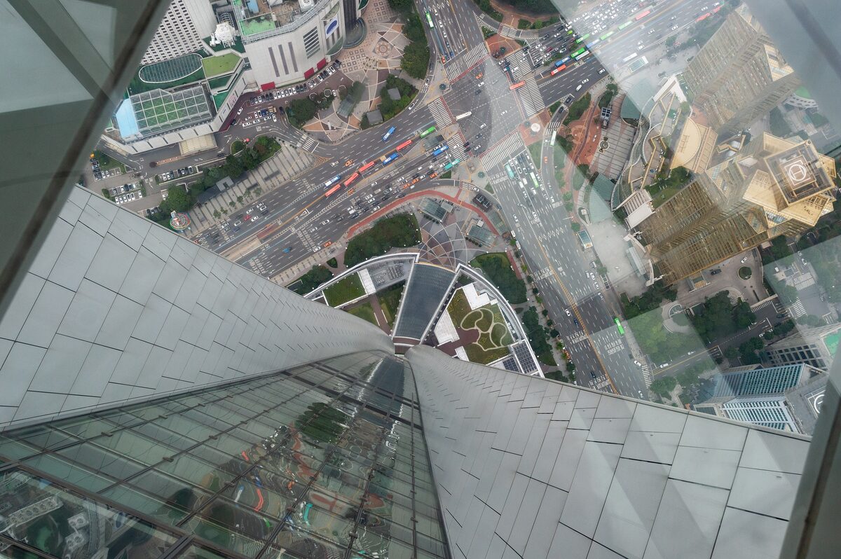 Looking straight down through the glass floor of the Lotte World Tower observation deck at the tower's slanted facade and the busy crossing far below