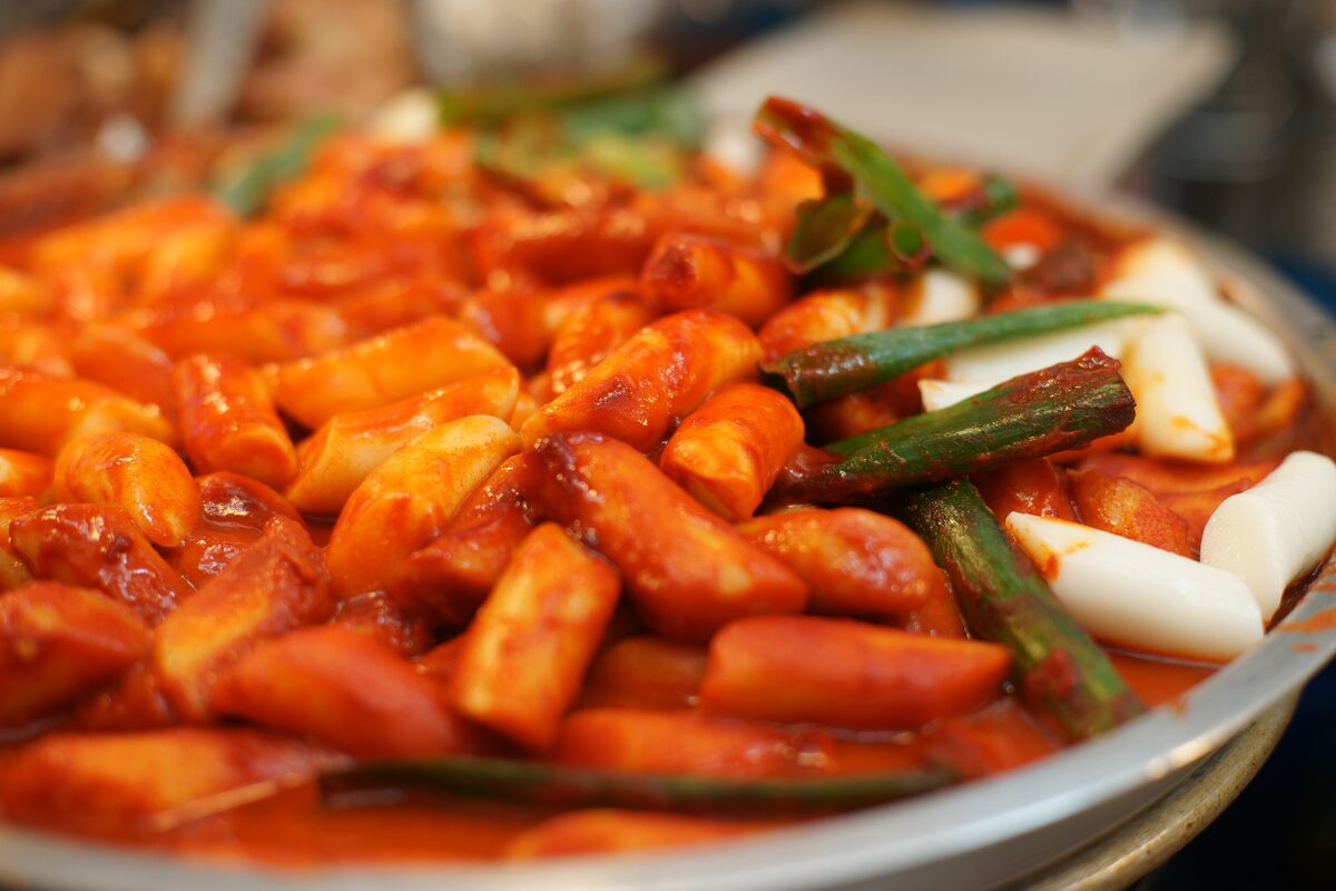 A pan of tteokbokki, chewy rice cakes in a red chili sauce with scallions