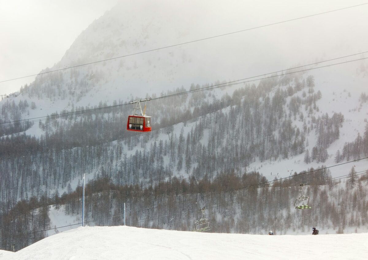 A red cable car cabin over a snowy, forested slope above the valley in light snowfall