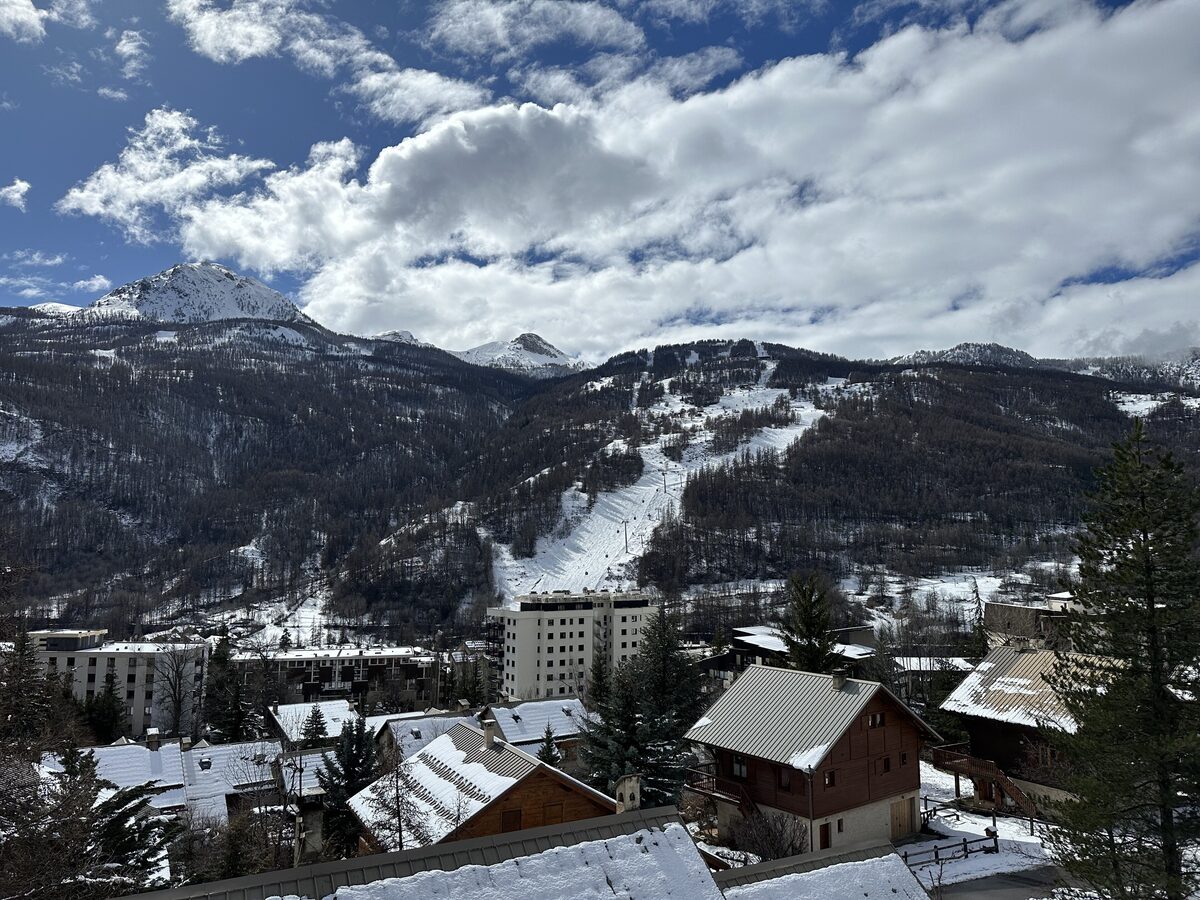 Resort buildings in snow below a ski piste on the hillside in the Saint-Chaffrey valley