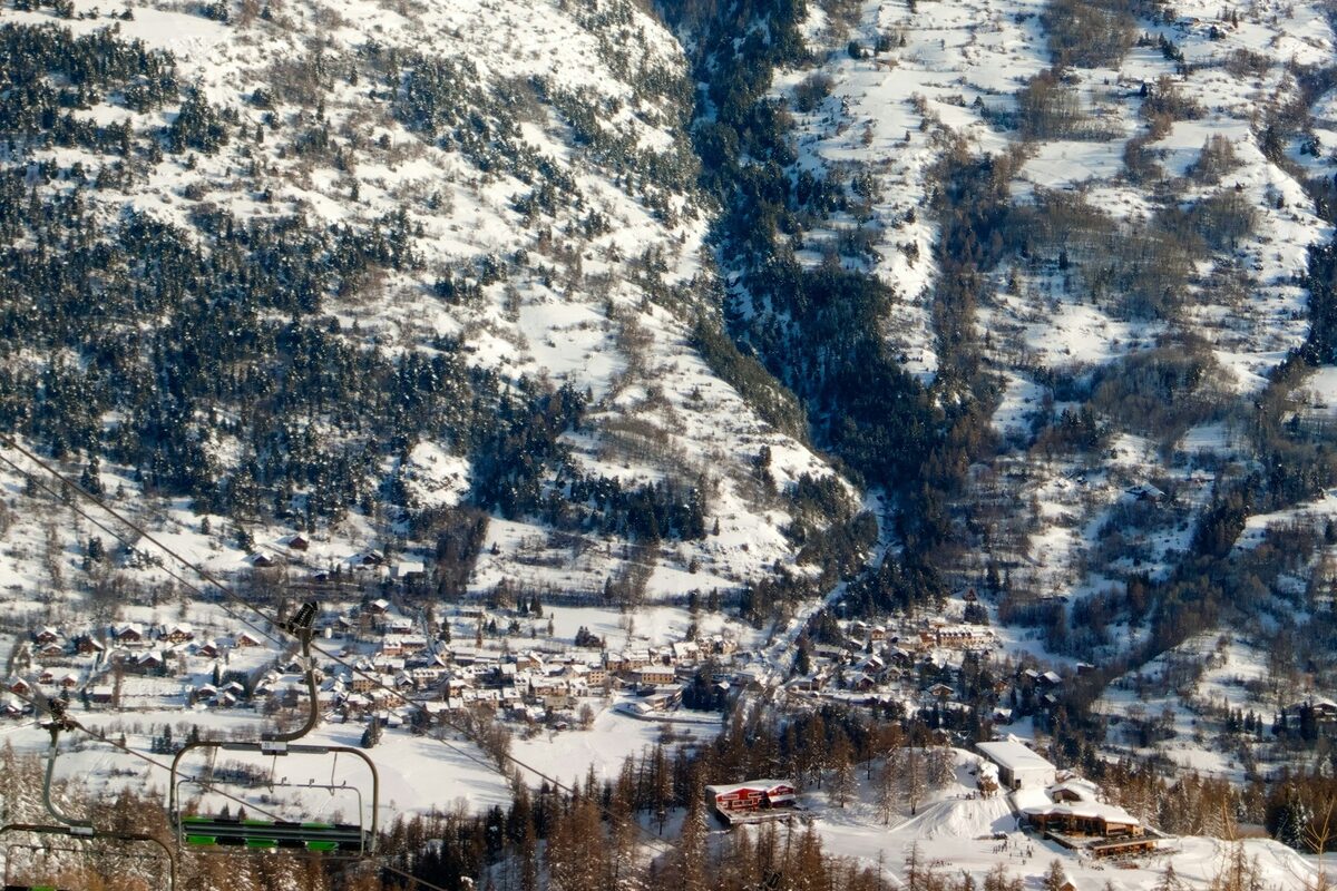The snowy villages of La Salle-les-Alpes in the valley, seen from a chairlift, with forested slopes above