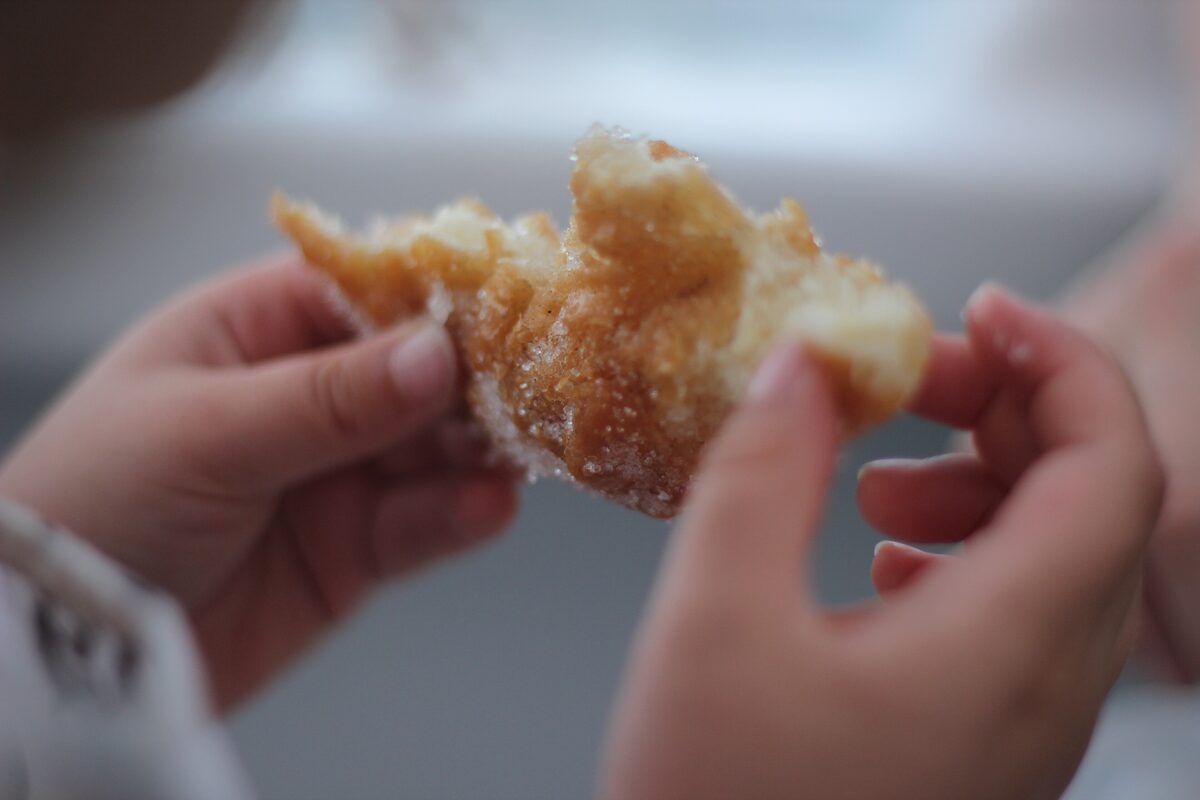 Hands breaking a golden sugared chichi fregi, a crisp fritter