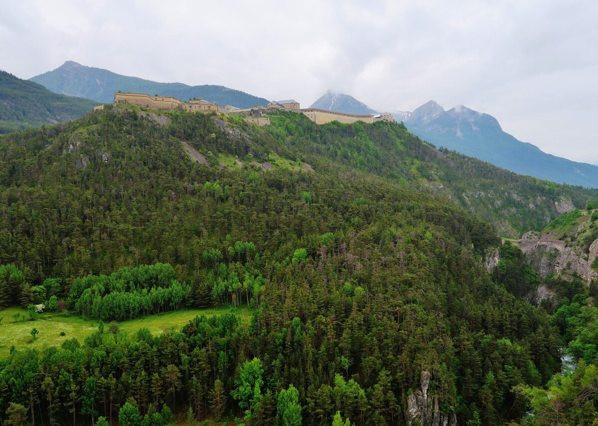 The Fort des Têtes, a long fortress on a ridge above the forest, with mountains behind