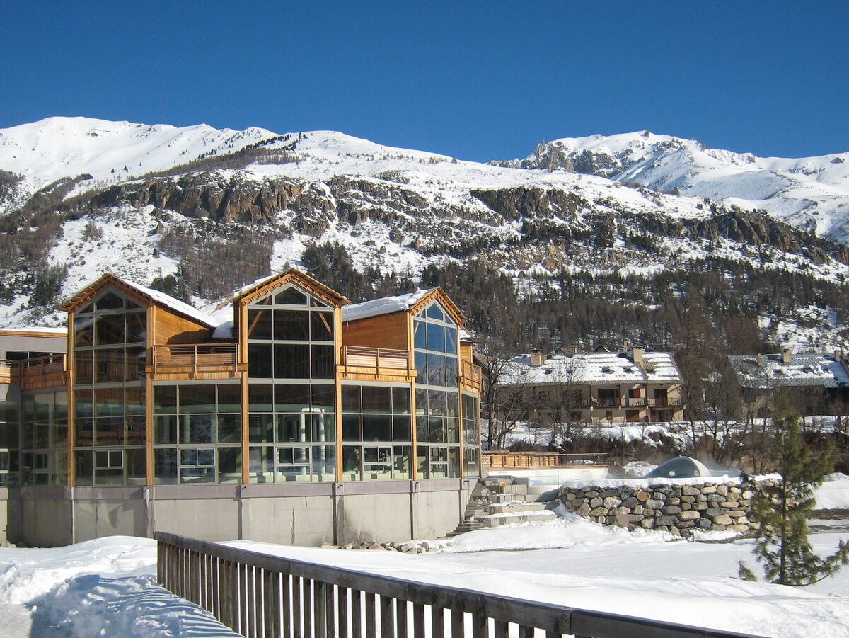 The Grands Bains du Monêtier thermal spa with its glass front, in snow under the mountains