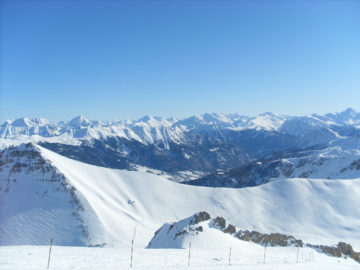 Snowy ridges and a wide valley seen from the high slopes of the Serre Chevalier ski area in bright sun