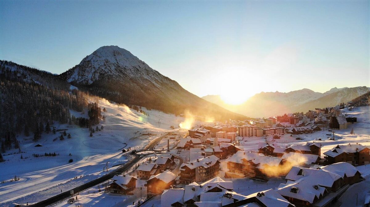 Montgenèvre at sunrise, with snow on the roofs and snow cannons running on the slope above the village