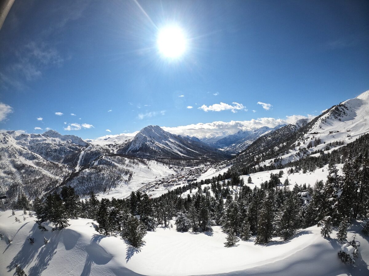 Snowy pines above a sunlit valley with the Montgenèvre resort far below