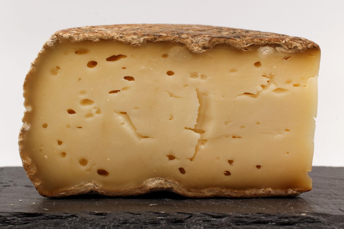 A wedge of Tomme de Savoie with a pale rind and small holes in the paste
