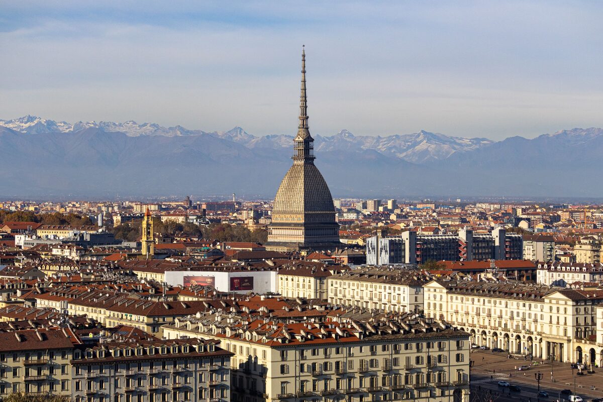 Turin's rooftops and the Mole Antonelliana tower, with the Alps on the horizon under a clear sky
