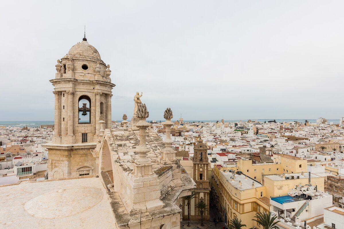 View over the white rooftops of Cádiz from the cathedral, with a domed bell tower in front and the sea beyond