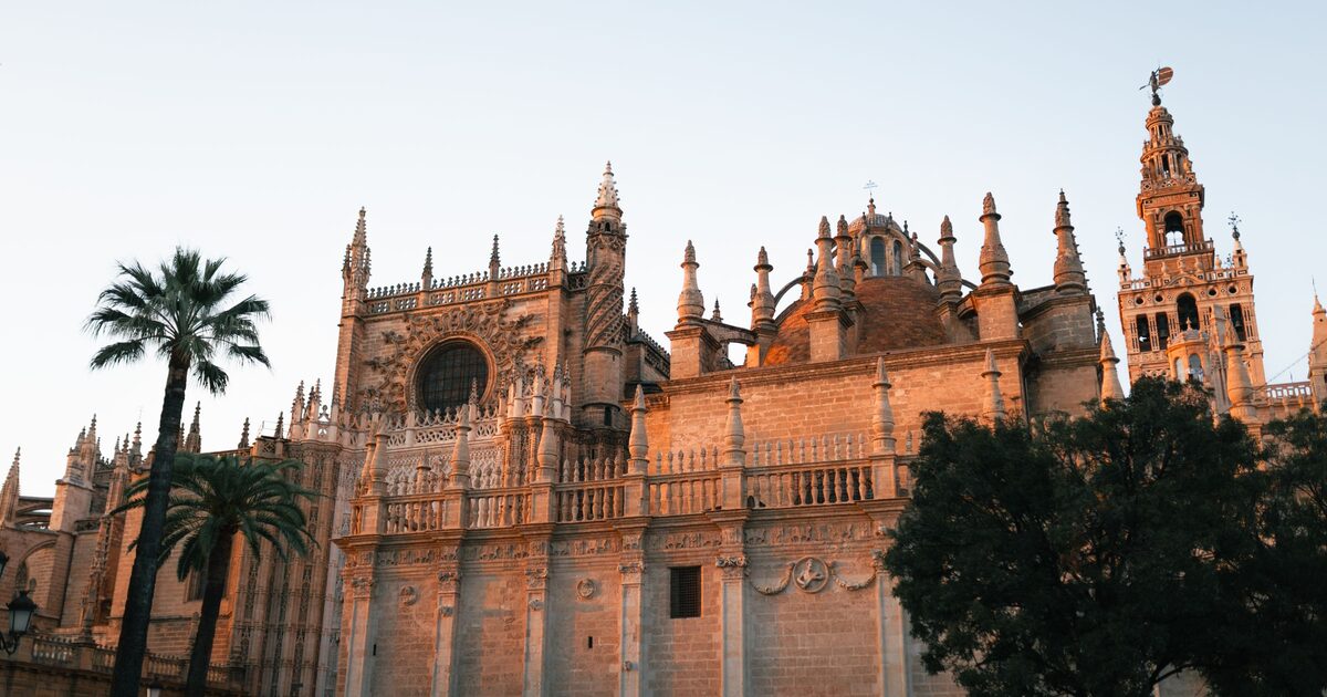 Seville Cathedral glowing orange in the evening light, with palm trees in front and the Giralda tower on the right