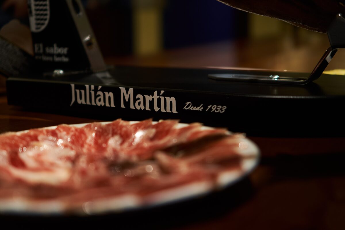 A plate of thinly sliced jamón ibérico on a bar counter, with a ham knife and a stand behind
