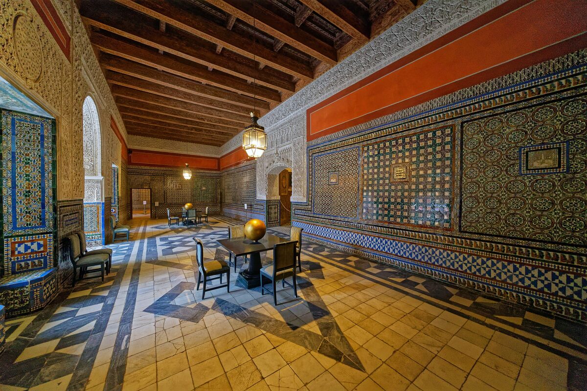 A long hall in the Casa de Pilatos with walls covered in geometric tiles, a coffered wooden ceiling and a tiled floor