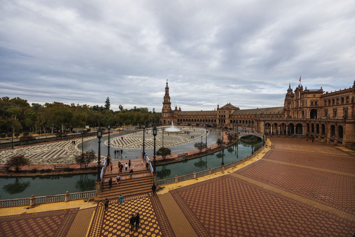 The huge semicircular Plaza de España in Seville, with its brick arcades, tower and canal under a cloudy sky