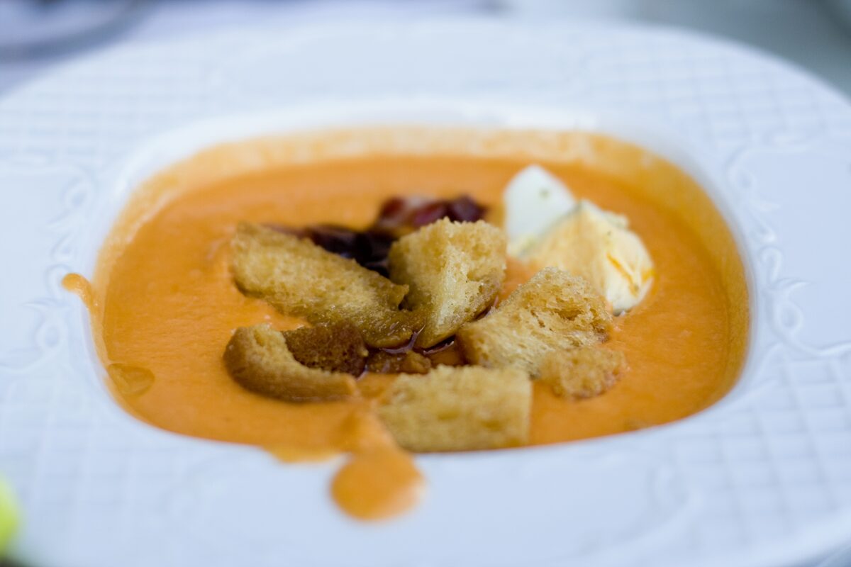 A bowl of orange salmorejo topped with croutons and a dollop of cream