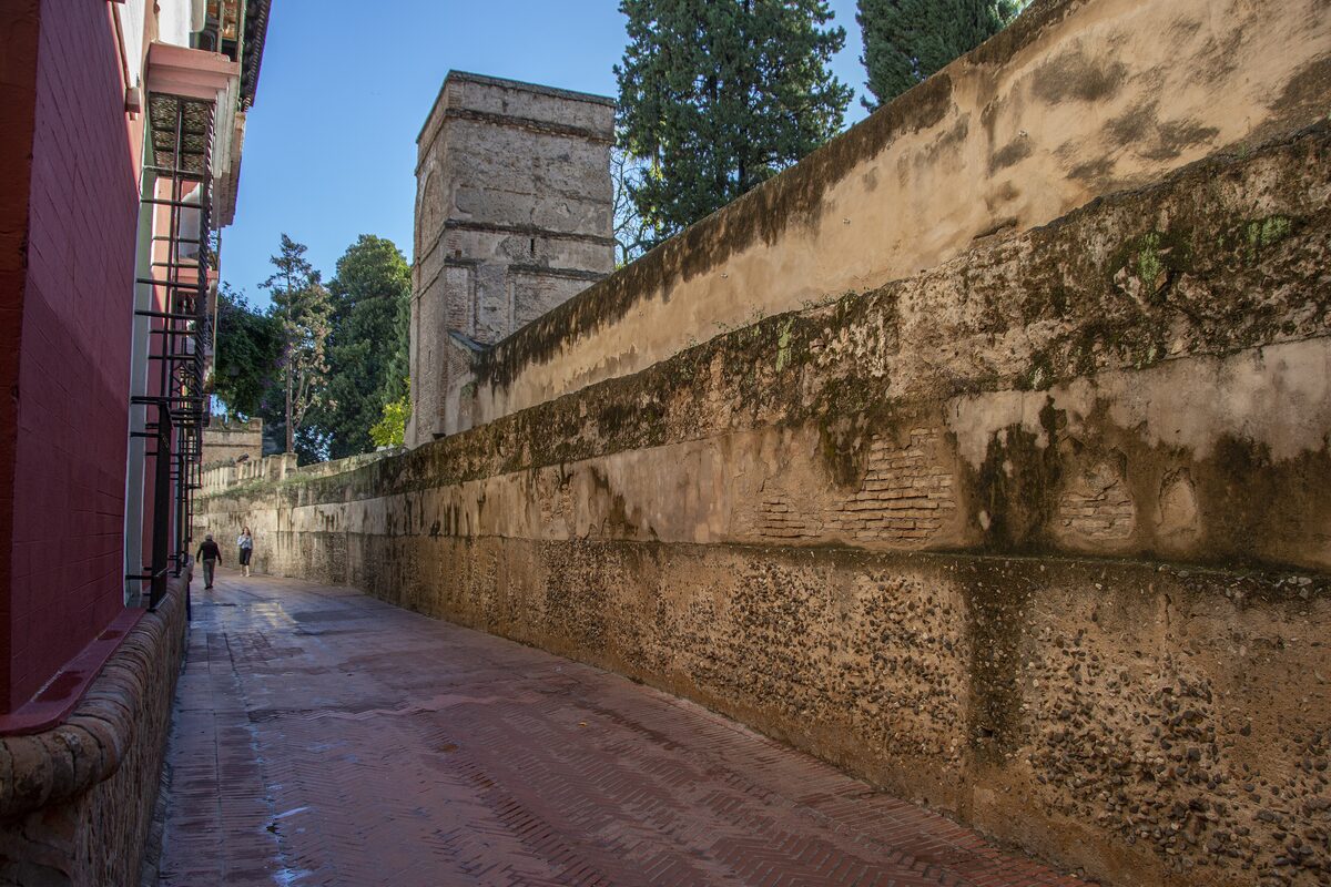 The narrow Callejón del Agua in Santa Cruz, a lane between an old wall and houses, with trees beyond the wall