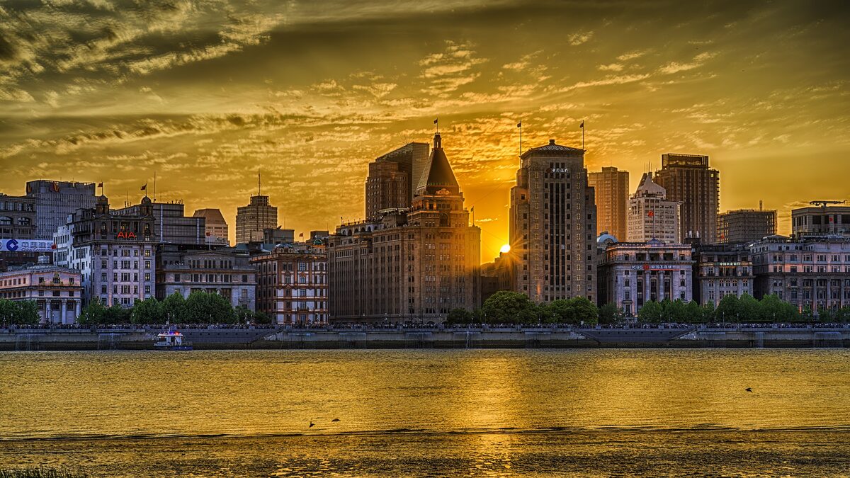The old bank and hotel buildings of the Bund glowing at sunset across the Huangpu River