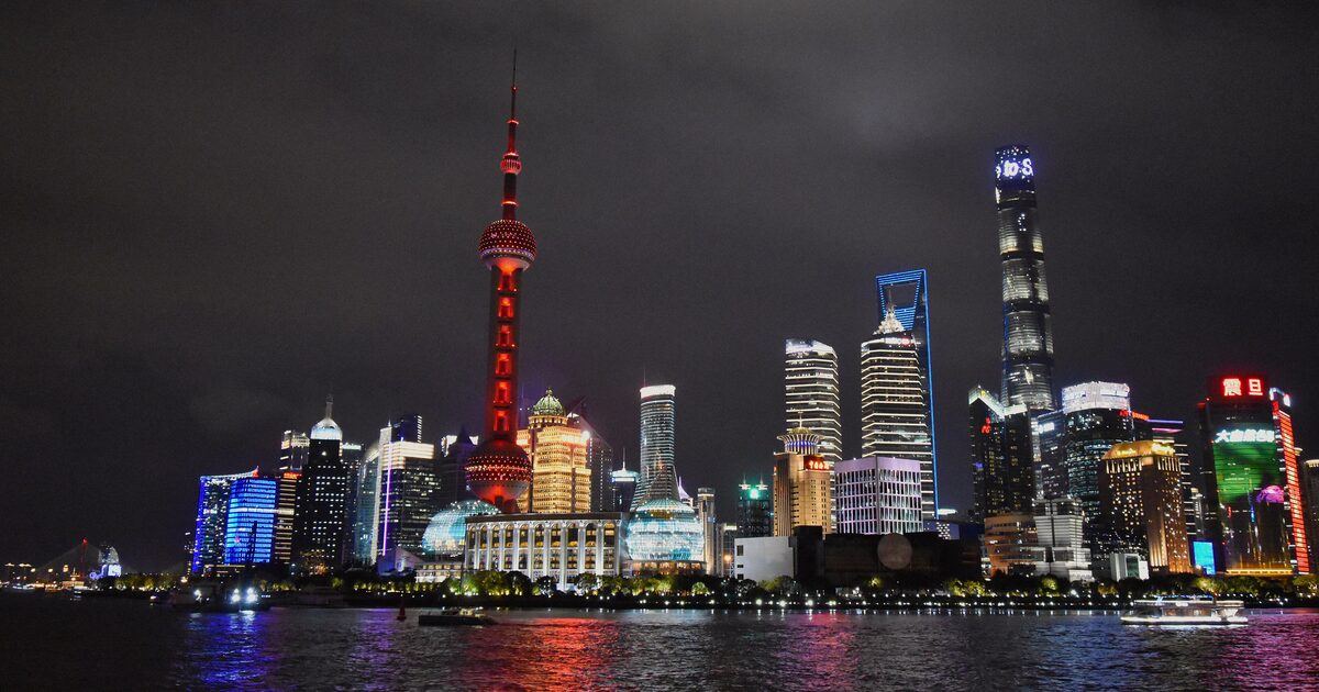 The Lujiazui skyline lit up at night across the Huangpu River, with the red-lit Oriental Pearl Tower and the Shanghai Tower