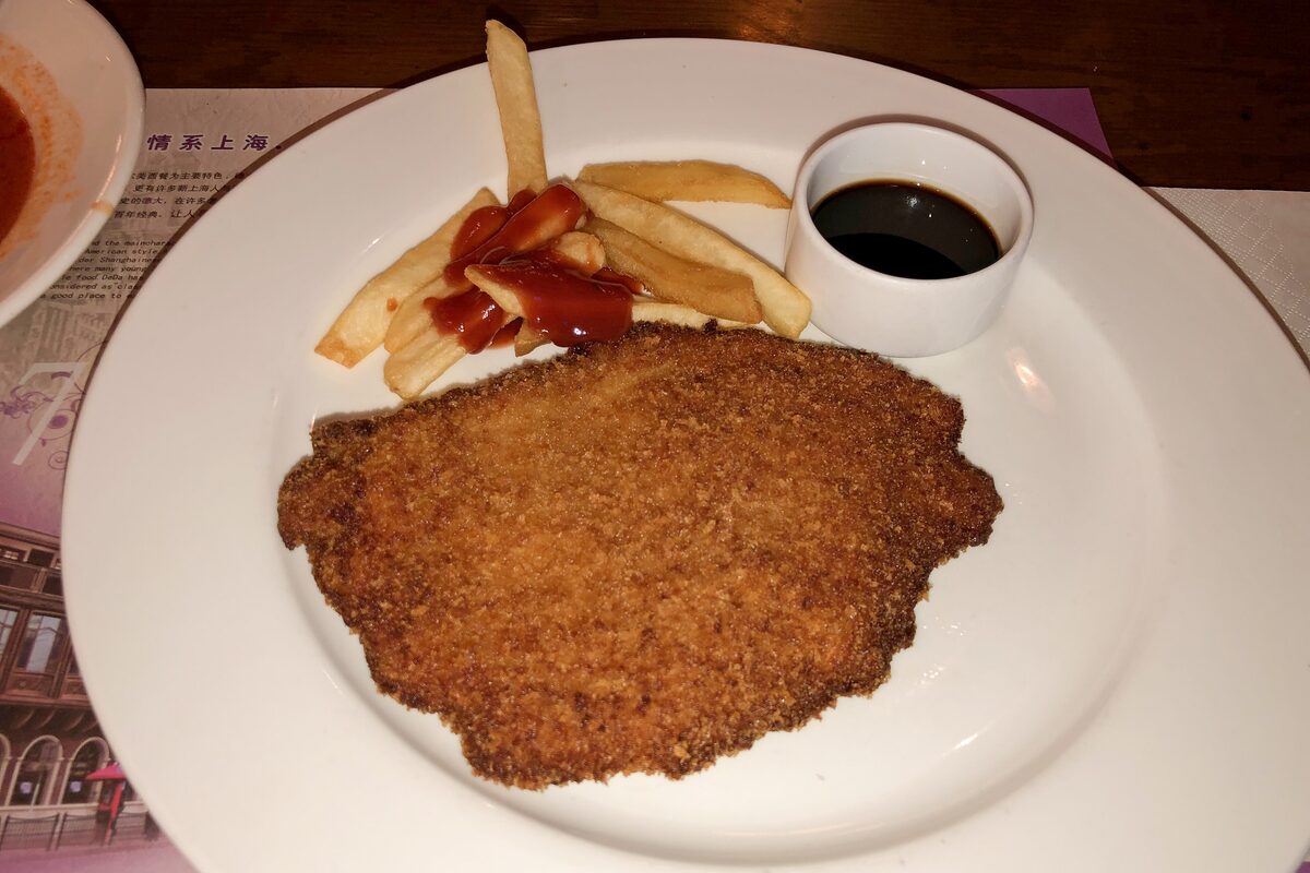 A breaded Shanghai-style pork chop on a plate with chips and a small cup of dark sauce