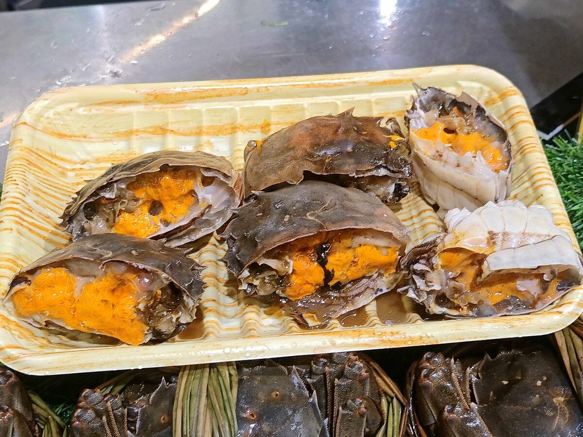 Halved hairy crabs with bright orange roe on a tray, with more crabs tied in grass behind