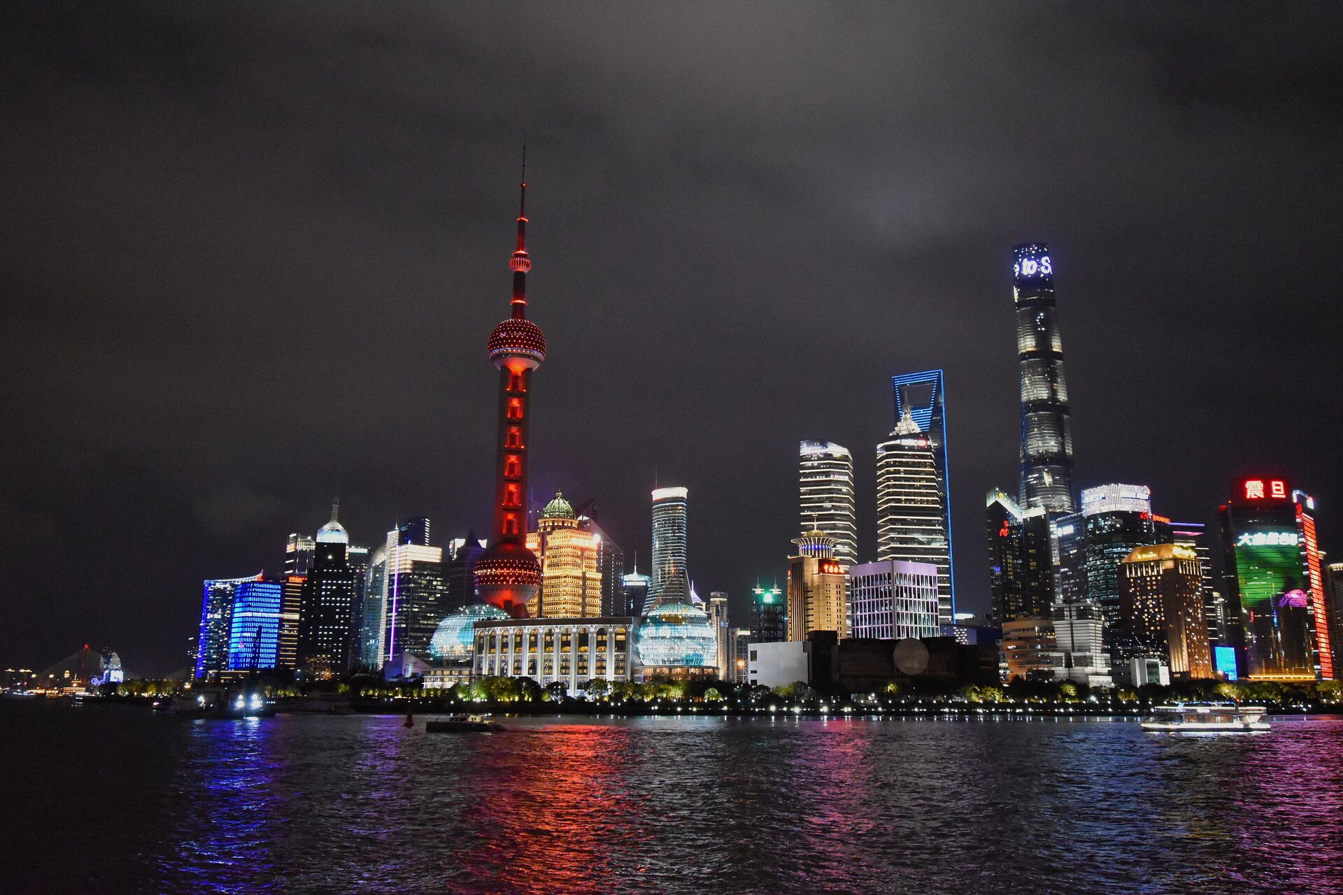 The Lujiazui skyline lit up at night across the Huangpu River, with the red-lit Oriental Pearl Tower and the Shanghai Tower