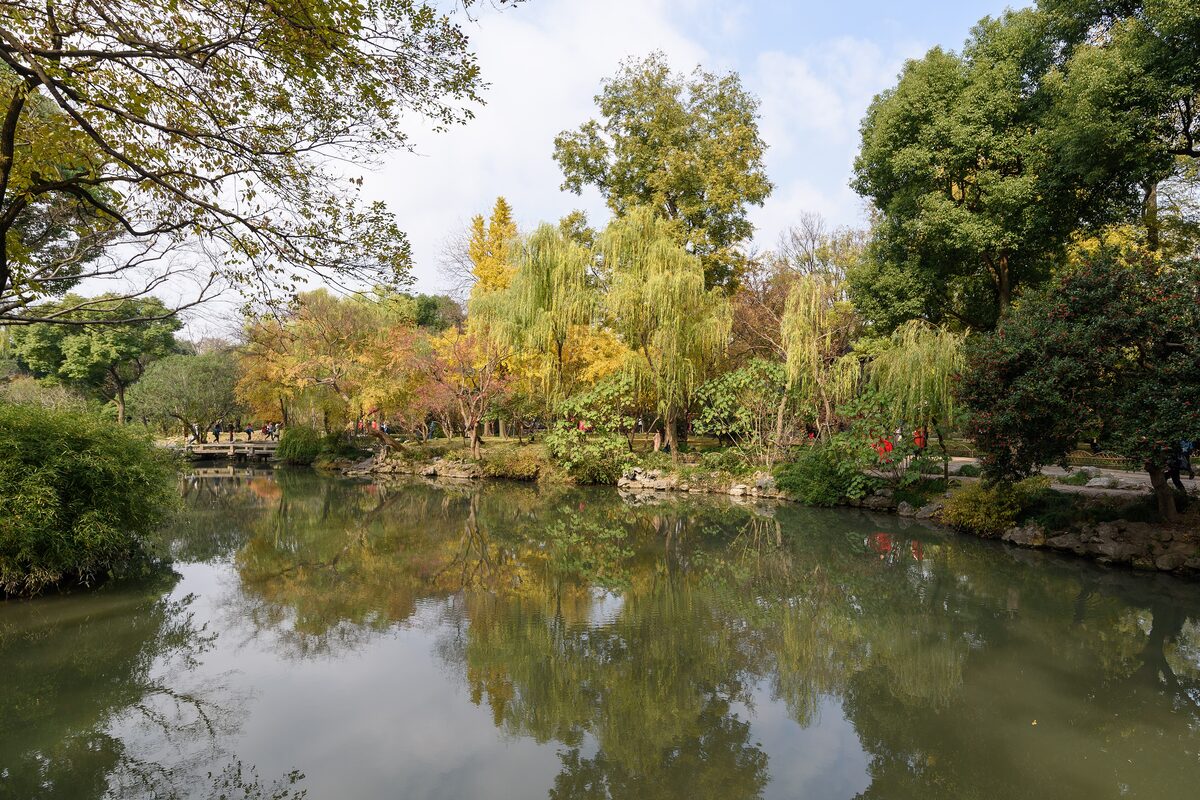 A still pond ringed by trees in autumn colors in the Humble Administrator's Garden