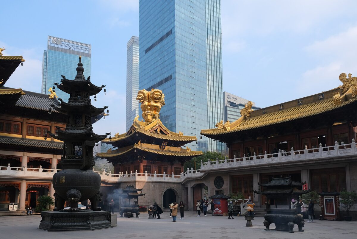The gilded roofs of Jing'an Temple's halls and an incense burner in the courtyard, with glass towers behind