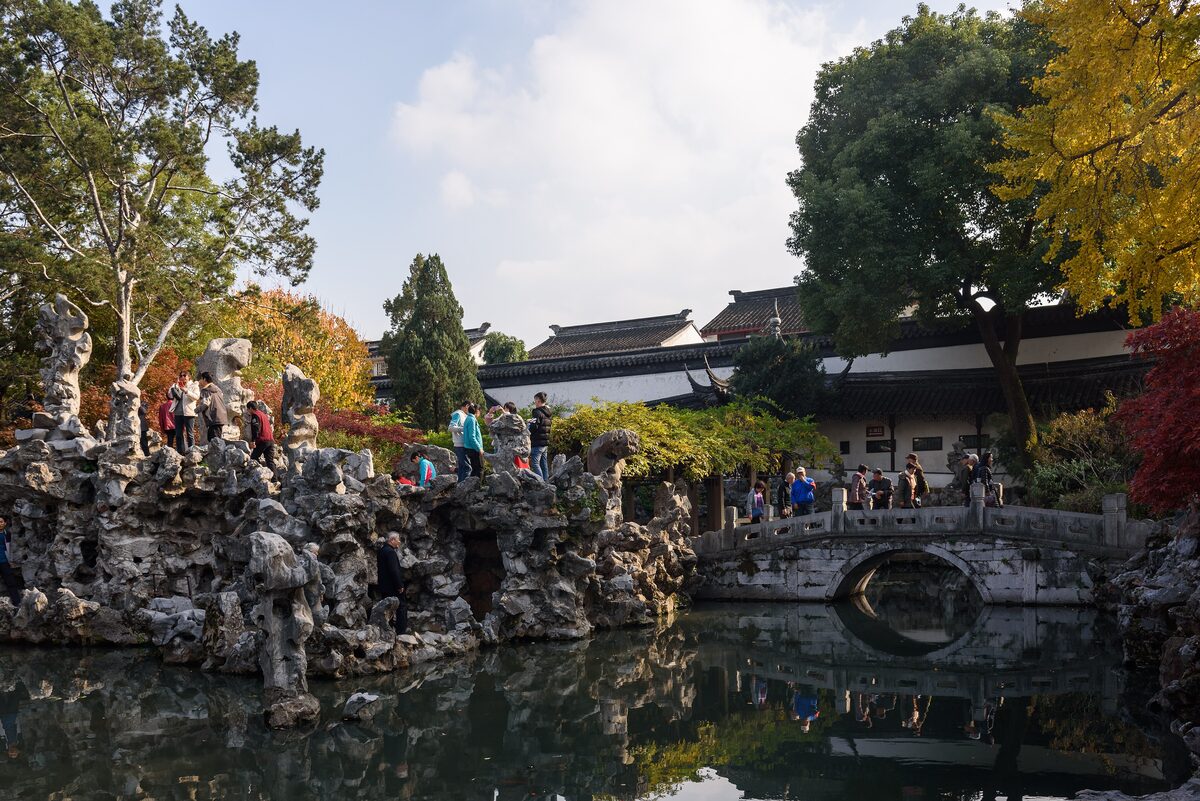 Rockwork and a small arched stone bridge over a pond in Lion Grove Garden, with autumn trees around
