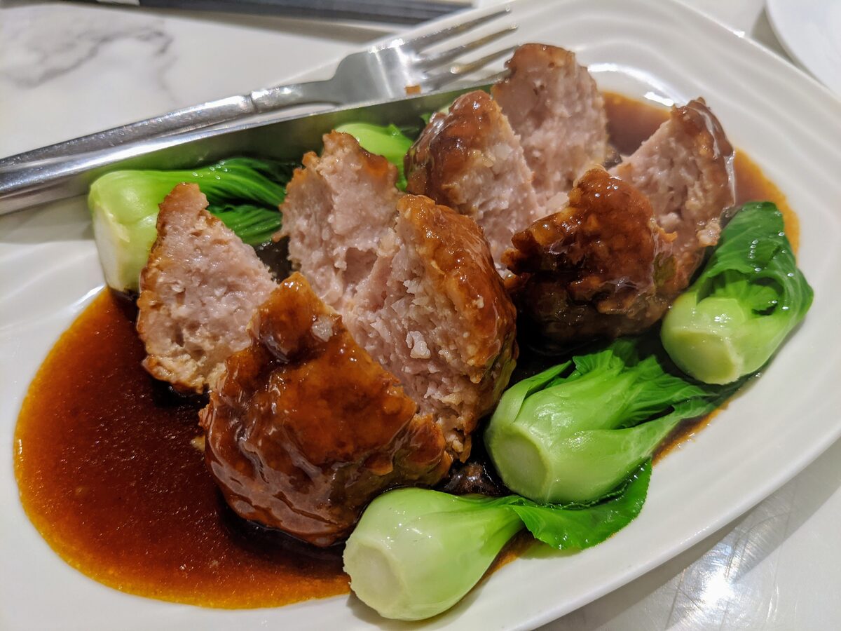 Large braised pork meatballs in brown sauce on a bed of bok choy