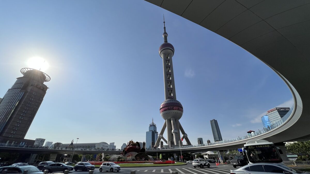 The Oriental Pearl Tower seen from the street under a curving elevated walkway, with glass towers around it