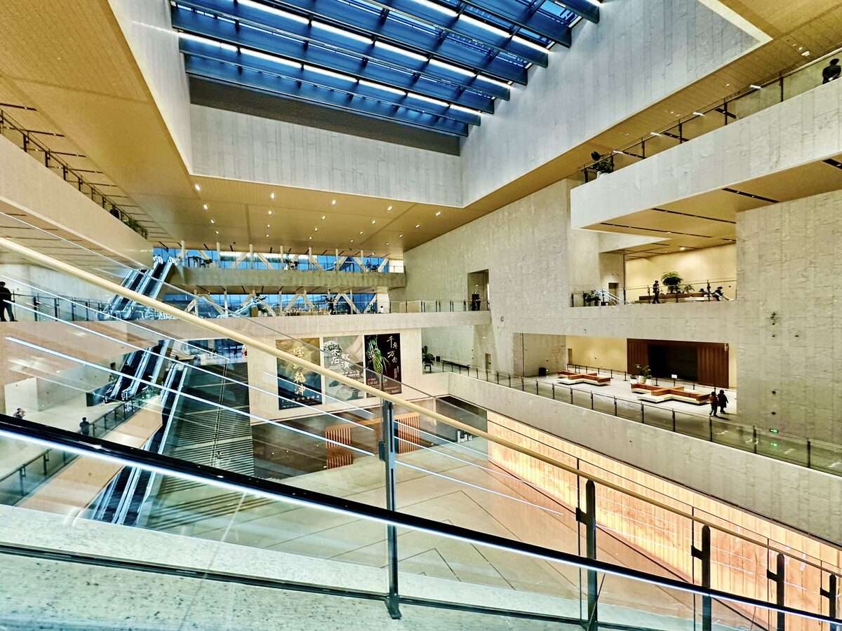 The bright atrium of Shanghai Museum East, with escalators, pale stone walls and a glass roof