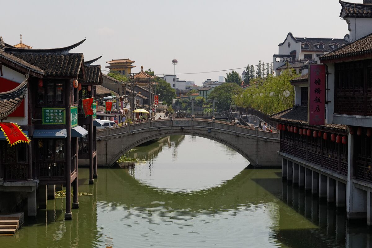 A stone arch bridge over the Qibao canal, with timber teahouses, red lanterns and tiled roofs along the water