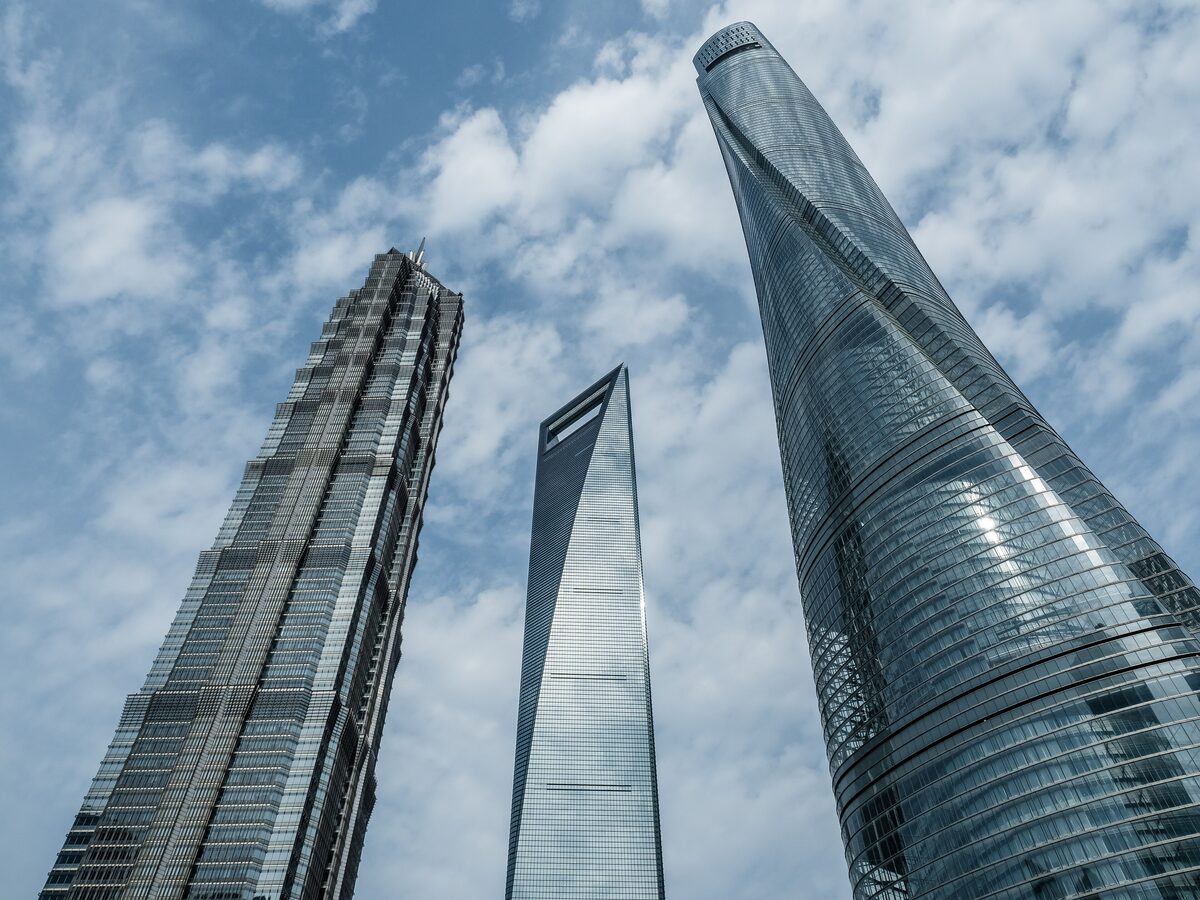 Looking up at the twisting Shanghai Tower beside the Shanghai World Financial Center and the Jin Mao Tower under a cloudy sky