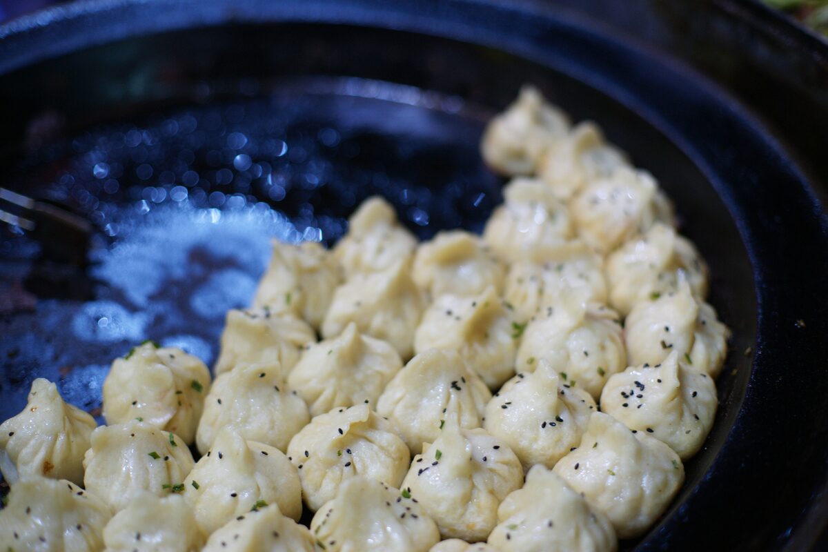 Pan-fried pork buns sprinkled with black sesame seeds in a large flat pan