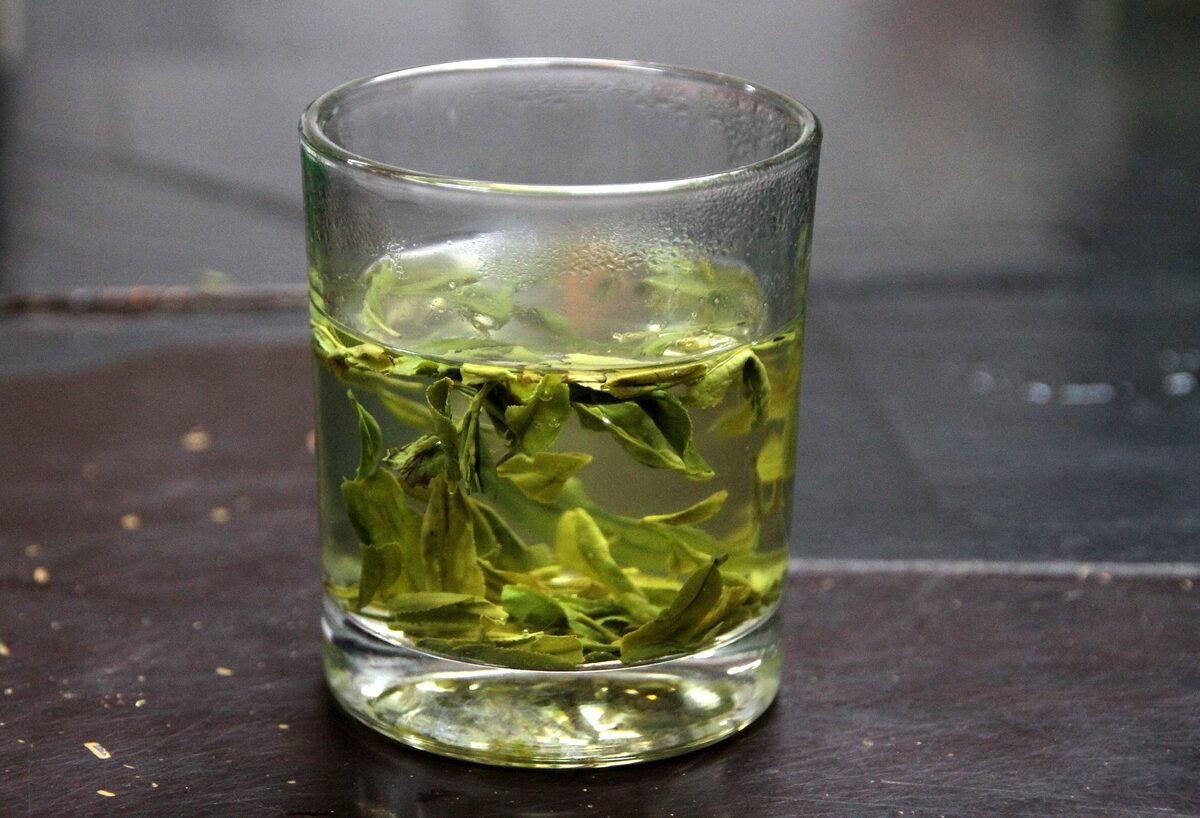 A glass of Longjing green tea with the leaves unfurled, from the tea hills near Hangzhou