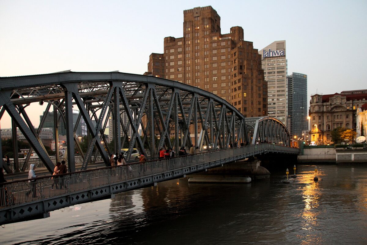 The steel Waibaidu Bridge over Suzhou Creek at dusk, with a tall brick building behind it