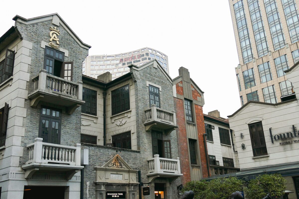 Grey-brick shikumen-style buildings with balconies and shops in Xintiandi, with a glass tower behind
