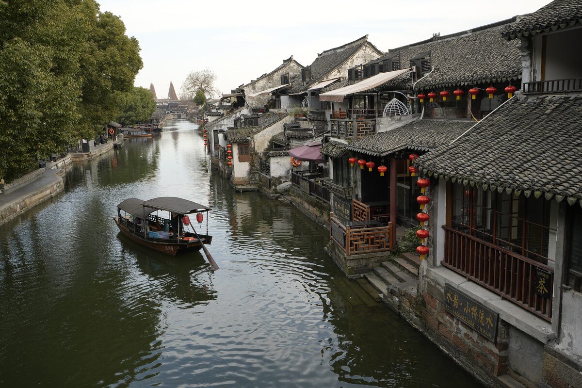 A canal in Xitang lined with tiled-roof wooden houses and red lanterns, with a covered boat on the water