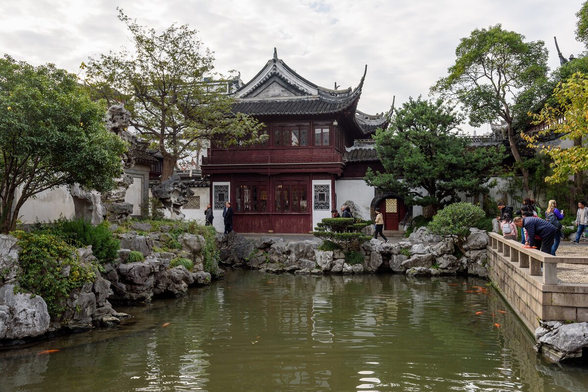 A two-story pavilion with upturned eaves across a pond, with rockwork and a stone railing in Yu Garden