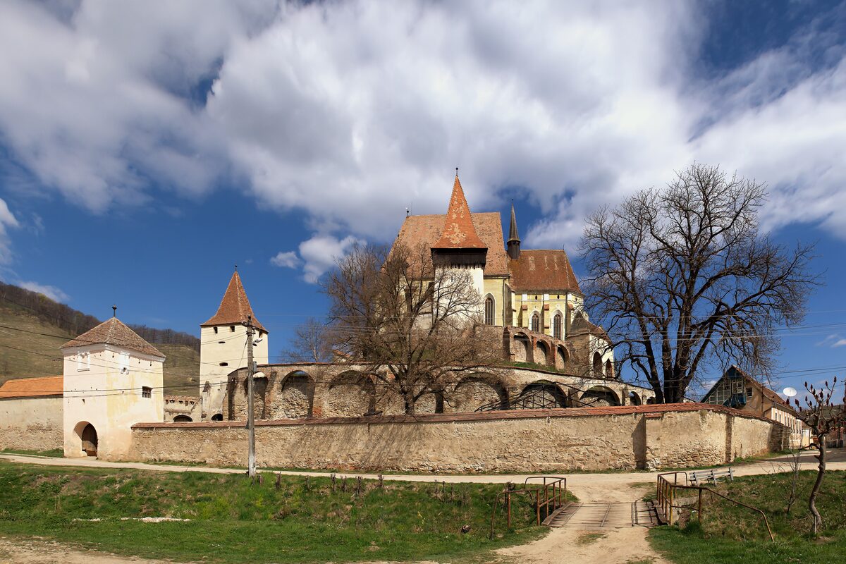 The fortified church of Biertan on its hill, ringed by stone walls and towers with red roofs, under a dramatic sky