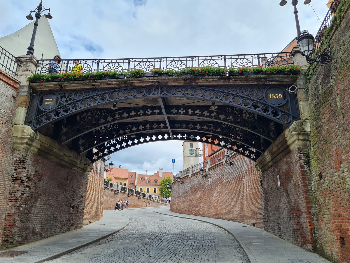The cast-iron Bridge of Lies, dated 1859, arching over the cobbled Strada Ocnei between brick walls, seen from below