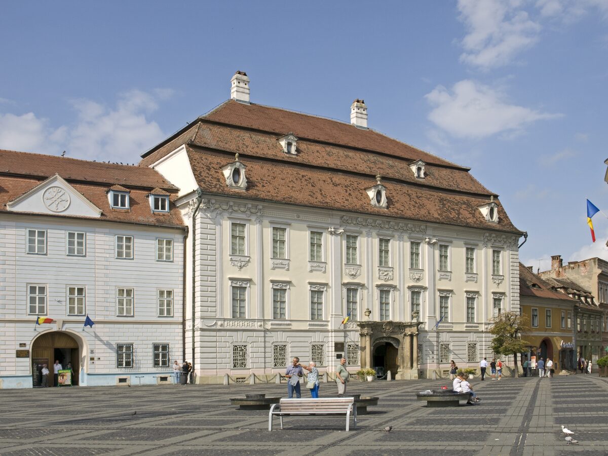 The pale baroque facade of the Brukenthal Palace on Piața Mare, with its carved stone portal and eyelid dormers in the roof