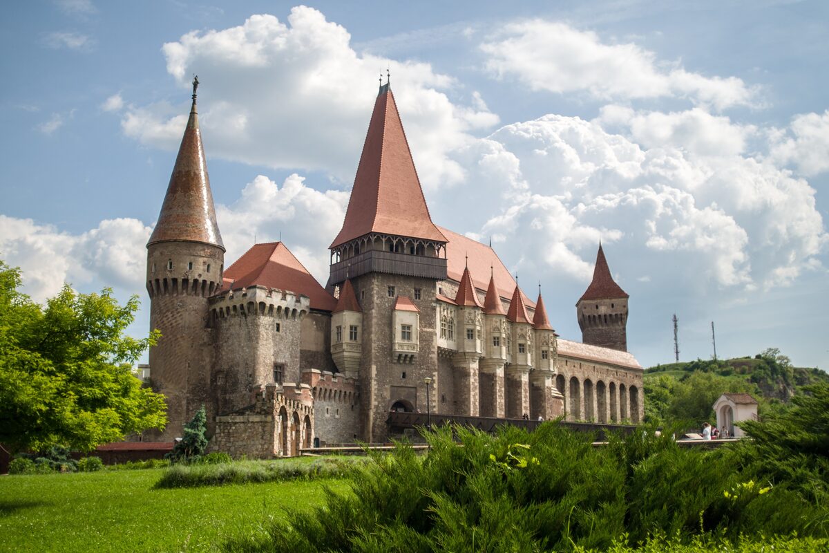 Corvin Castle in Hunedoara, with its tall pointed red-roofed towers and Gothic walls, under white clouds