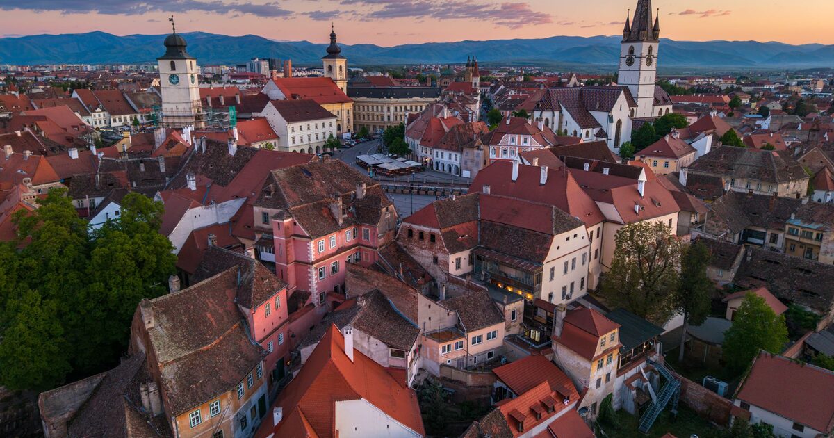 Sunset over the red rooftops of Sibiu's old town, with the Council Tower, the Lutheran Cathedral's spire and the Făgăraș Mountains on the horizon
