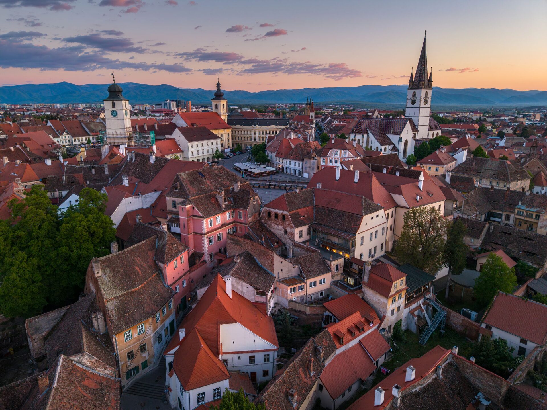 Sunset over the red rooftops of Sibiu's old town, with the Council Tower, the Lutheran Cathedral's spire and the Făgăraș Mountains on the horizon